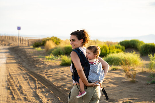 Mother walking while carrying a baby on her back in a baby carrier outdoors