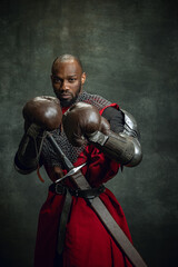 Vintage style portrait of brutal dark skinned man, medieval warrior or knight wearing armour in...