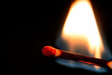 Flame burns in wooden match on dark background