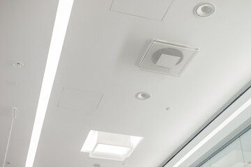 White plasterboard ceiling in administrative and public building with ventilation, lamps and speakers