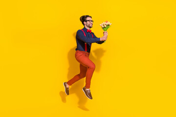 Fototapeta na wymiar Full size profile side photo of young guy jump up hold bunch of tulips present look empty space isolated over yellow color background
