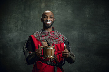 Cheerful man in image of medieval warrior, knight wearing war armor holding big mug of frothty...