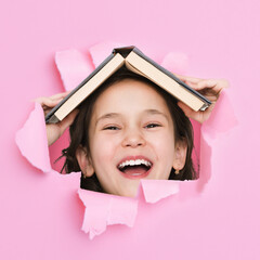 Happy excited pretty cute asian little girl with open mouth and books on her head looks through...