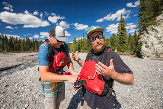 Two men work to strap on lifejackets while paddling.