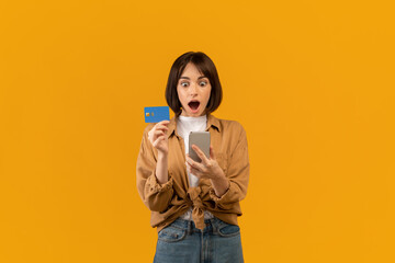 Bonus and cashback concept. Surprised young lady showing debit credit card, using smartphone,...