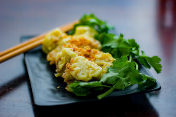 Chinese Steamed Dumpling served in a black plate on a wooden table. along with cilantro.