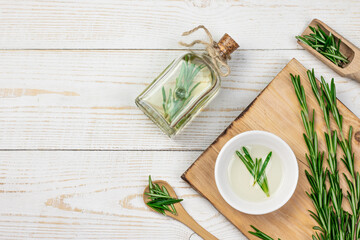 Aromatherapy rosemary oil. Wooden board, Bottle glass with rosemary essential oil, little spoon and fresh rosemary twig on white background.