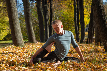 Sporty man practicing yoga in autumn park