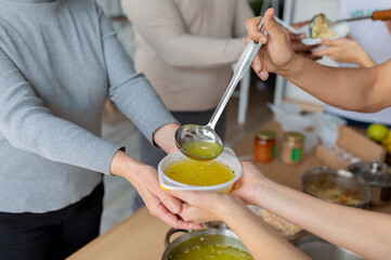 Help for aged people. Young volunteers serving hot soup for elderly or homeless in charity donation center, closeup
