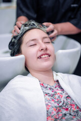 Professional hairdresser washing hair of a little girl in hair salon.