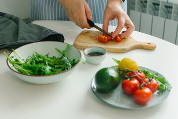 Woman preparing vegetable salad with tomato in the kitchen. Healthy food vegan salad. Mindful eating