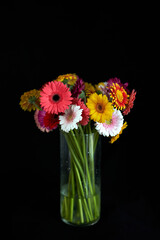 Florist or botanical theme. Beautiful bouquet of yellow, red, white and pink flowers in glass vase isolated on black background. 8 march, valentine's day or International women's day concept