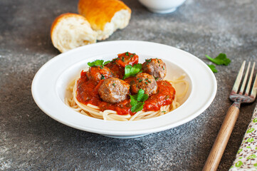 Spaghetti with meatballs and tomato sauce in a white plate on a gray background.