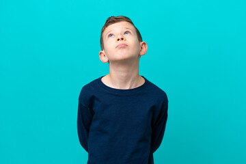 Little kid boy isolated on blue background and looking up