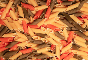Full frame closeup of many raw cylinder shaped penne rigate pasta noodles in three colors yellow, green and red