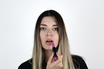 Close up photo of charming girl hold purple pomade. She check new lips stick matte effect isolated over white background. Cosmetic, beauty and make up.
