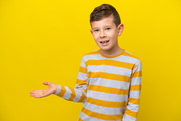 Little caucasian boy isolated on yellow background presenting an idea while looking smiling towards