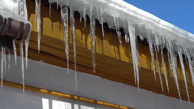 The roof of the building is covered with snow and ice after a snowfall. Hanging and falling icicles are a danger to people. Icy drainpipe on a sunny and frosty day.