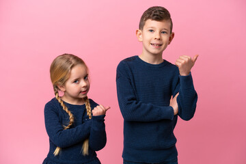 Little caucasian brothers isolated on pink background pointing to the side to present a product