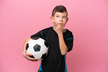 Little caucasian football player boy isolated on pink background having doubts