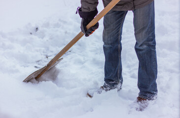 a man cleans the street from snow with a special flat shovel. winter seasonal yard cleaning and activity.