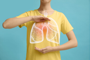 Woman holding hands near chest with illustration of lungs on turquoise background, closeup