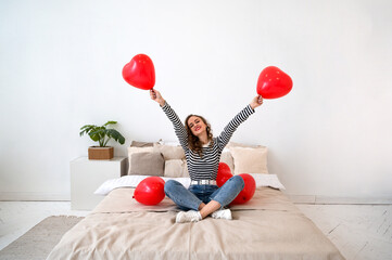 Valentine's Day. Young happy female on the bed with red heart shaped balloons