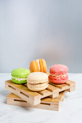 Sweet and colourful macaroons served on little wooden pallets on a marble texture table and silver...