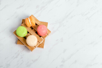 Sweet and colourful macaroons served on little wooden pallets on a marble texture table. Traditional french dessert. Copy space.