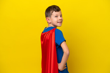 Little caucasian boy isolated on yellow background in superhero costume and doingposing with arms at hip and smiling