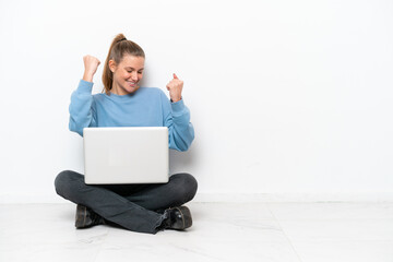 Young woman with a laptop sitting on the floor celebrating a victory