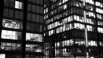 Obraz premium Amazing night cityscape. Office building at night, building facade with glass and lights. View with illuminated modern skyscraper. Scenic glowing windows of skyscrapers at evening. Black and white.