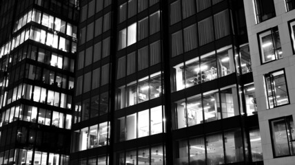 Obraz premium Amazing night cityscape. Office building at night, building facade with glass and lights. View with illuminated modern skyscraper. Scenic glowing windows of skyscrapers at evening. Black and white.