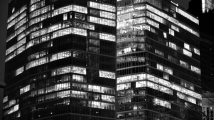 Fototapeta na wymiar Amazing night cityscape. Office building at night, building facade with glass and lights. View with illuminated modern skyscraper. Scenic glowing windows of skyscrapers at evening. Black and white.