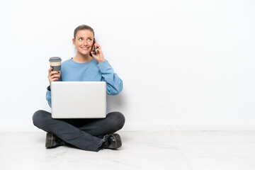 Young woman with a laptop sitting on the floor holding coffee to take away and a mobile