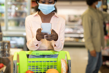 Black Female Doing Shopping Using Cellphone Wearing Mask In Supermarket
