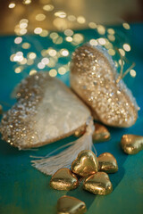 Chocolate candies in the form of hearts in gold foil. Blurred white hearts with bokeh on a green table. Wedding greeting card.