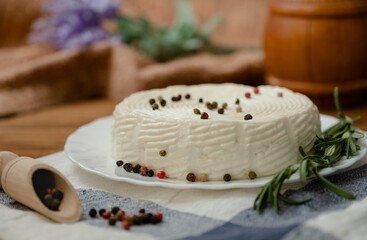 A head of cheese in a white plate lies on the table with blueberries and rosemary. Fresh goat cheese lies on a wooden table.