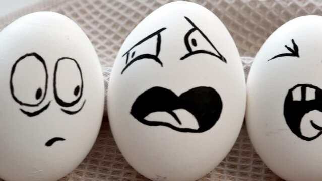 Boiled white eggs with funny emotional muzzles on a yellow background. Sliding the camera along a row of eggs. Easter.