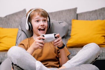 Teen boy with headphones and joystick playing video game console.