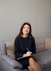 a business consultant woman is sitting on a gray sofa in a room. A Caucasian woman with papers is sitting on the couch and conducting an interview