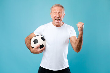 Mature man posing with soccer ball on blue background © Prostock-studio