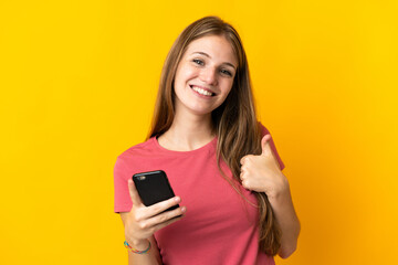 Young woman using mobile phone isolated on yellow background with thumbs up because something good...