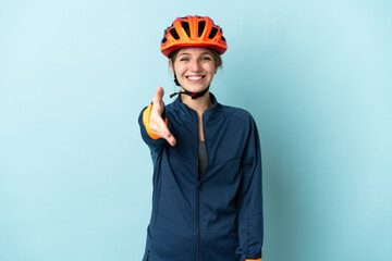 Young cyclist woman isolated on blue background shaking hands for closing a good deal
