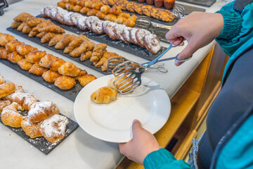 Woman selecting butter croissant at pastry counter in buffet restaurant