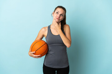 Young woman playing basketball isolated on blue background having doubts while looking up