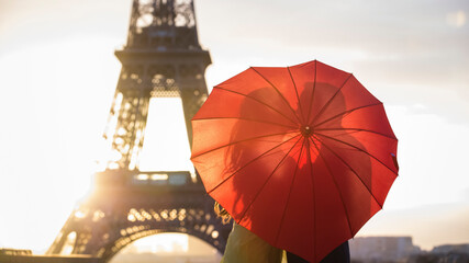 Romantic kiss at the Eiffel tower with a red umbrella during sunrise