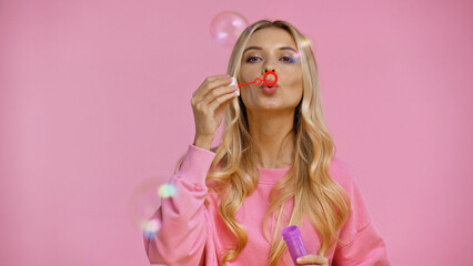 Naklejka premium Pretty woman blowing soap bubbles isolated on pink.