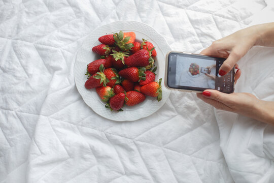 hands take pictures plate with strawberries  white bed