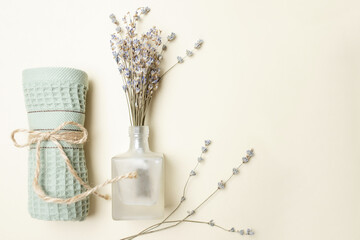 The concept of spa salon, bathroom decor, cozy home, feminine. Bouquet of natural dry lavender flowers in a glass bottle, rolled up towel. Top view. Copy space. Beige background.
